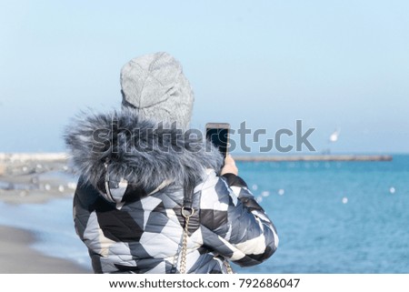 
A girl in winter photographs on the phone sea landscape
