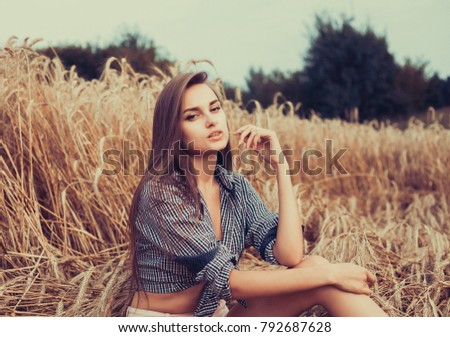 Attractive girl in checkered shirt and shorts resting in wheat field in summer

