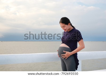 Beautiful pregnant woman standing on seashore with looking at her belly.