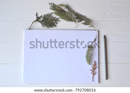 White paper and pencil with decoration on the white wooden desk, top view.