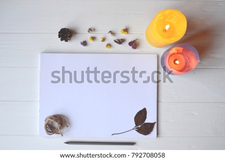 White paper and pencil with decoration on the white wooden desk, top view.