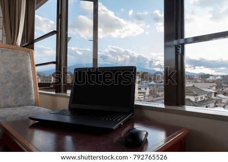 The notebook computer is located on a table near window with a view of the village and Mount Fuji as the background.