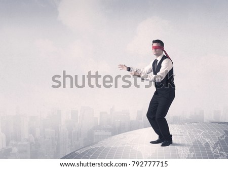 Young blindfolded businessman steps on a grey world map with a city in the background