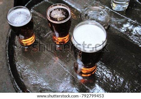 Three pints of lager beer viewed from above on a brown barrel outside of a pub or a bar, and an ashtray Royalty-Free Stock Photo #792799453