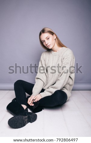 positive girl with long blonde hair wearing an old warm sweater and black pants. emotional portrait. posing in the Studio on a colored paper background. concept: woman farmer in her clothing