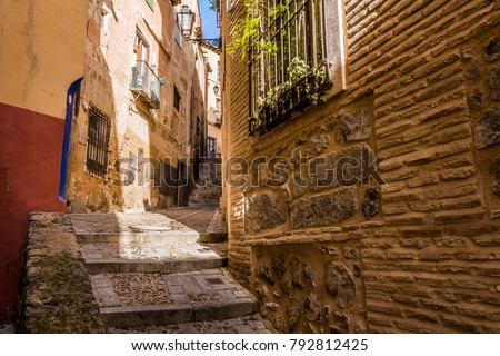 Medieval cobbled and stepped street with flowery balconies and public lighting lamps in the city of Toledo. Spain Royalty-Free Stock Photo #792812425