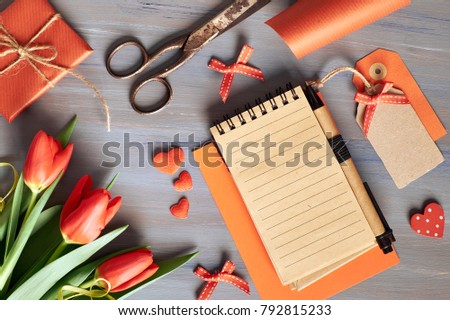 Blank notebook, wrapped gift, wrapping materials and fresh orange tulips on wooden table. Concept for a recepie or to do list for Spring celebration. Text space.