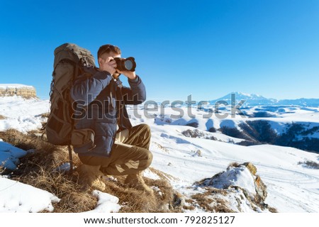 Portrait of a bearded hipster, a photographer with a backpack and in sunglasses takes pictures of his DSLR