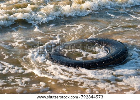Large rubber tire truck tire floats on the ocean shore, summer sunny day beach beach summer vacation weekend