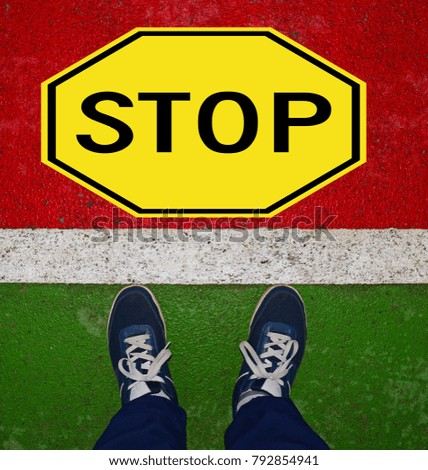Sneakers near the white line on a green background and a stop sign in yellow on a red background
