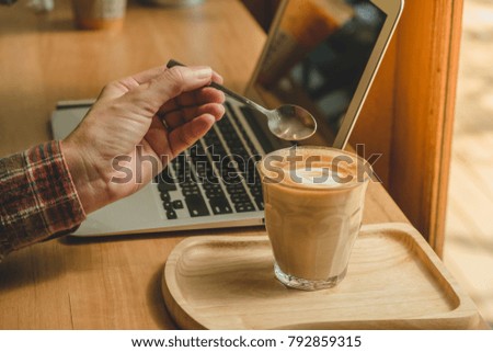 A cup of coffee latte with beautiful Latte art. On the wood table near a notebook with the sunlight.