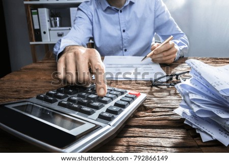 Close-up Of A Businessperson's Hand Calculating Invoice With Calculator At Workplace