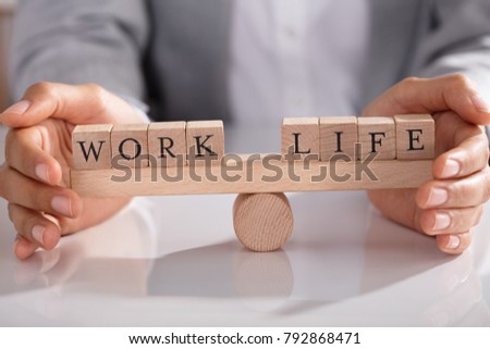 Businessperson's Hand Covering Balance Between Life And Work On Wooden Seesaw In Office Royalty-Free Stock Photo #792868471