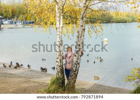 A woman stands between the birches on the lake shore
