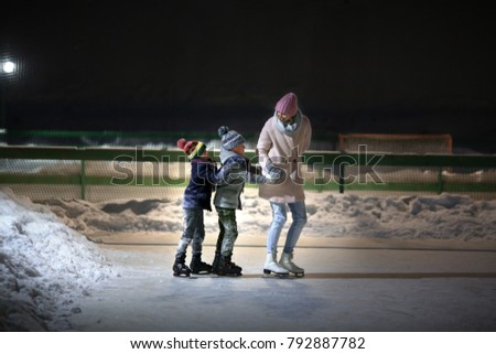 young mother teaching her little sons ice skating at outdoor skating rink