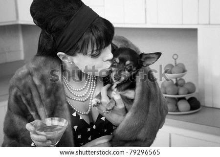 Middle-aged woman in fur coat with martini kisses a Chihuahua dog