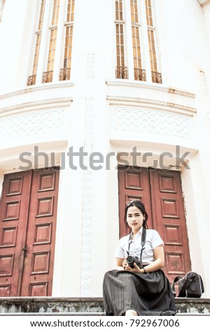The Girl hold the DSLR camera and sitting on the floor in front of the old door. 