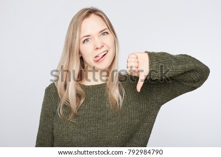 European woman shows disapproval sign, gives thumb down gesture, dislikes something, has disgusting expression, isolated over white background. Negative human expression and body language concept.