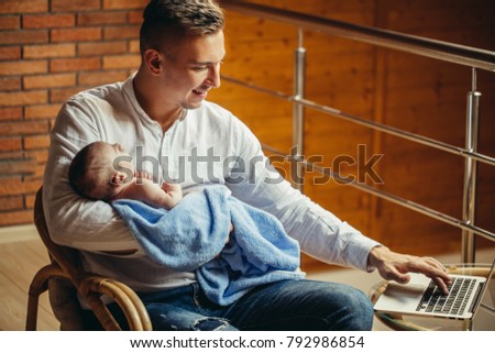 Father With Newborn Baby Working From Home office Using Laptop