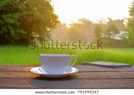 A front selective focus picture of a farmer's coffee cup in the morning sunrise beside rice field.