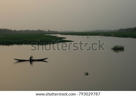 Silhouette of a lonely fisherman in his small wooden boat on a calm river. Colorful picture with sunset in the nature. Peaceful image of a pirogue and a man fishing in the evening in Africa.  