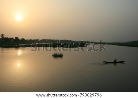 Silhouette of a lonely fisherman in his small wooden boat on a calm river. Colorful picture with sunset in the nature. Peaceful image of a pirogue and a man fishing in the evening in Africa.  