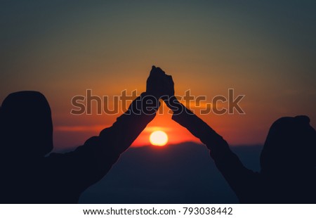 Silhouette of man and woman are standing on top of the mountain with raised hands relaxing with sunrise by nature at sunrise ,Life style,Happy couple in love at sunrise or sunset,First morning light, 