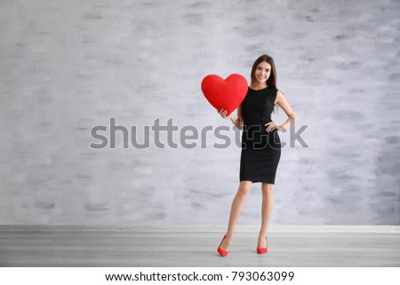 Romantic young woman with heart-shaped pillow indoors