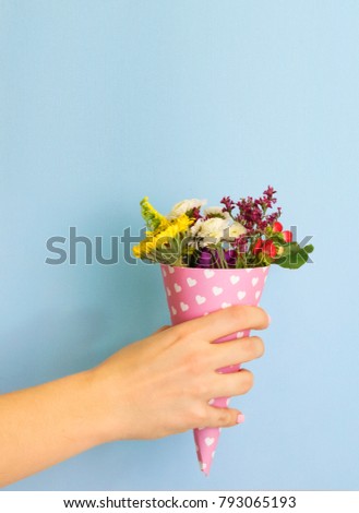 hand holds a bouquet of flowers in a paper horn with hearts on a blue background. a gift for St. Valentine's Day. gift for International Women's Day