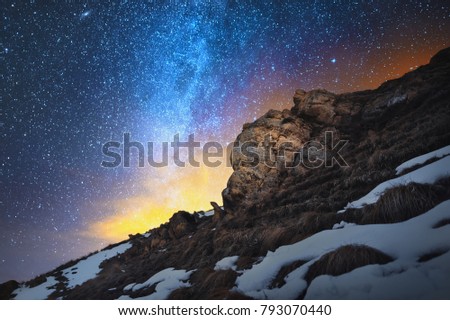 Night scenery done on long exposure. A beautiful Caucasian landscape of red rocks against the background of the cold milky way and a warm yellowish red glow on the horizon behind the rocks.