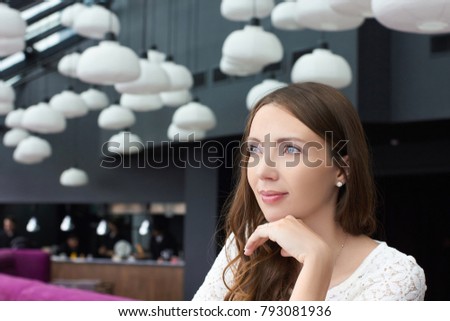 Beautiful caucasian woman dreaming about something while sitting in modern cafe bar. Young charming female freelancer thinking about new ideas. Young woman listens attentively to her interlocutor.