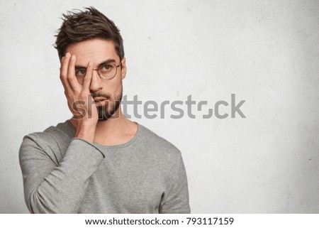 Photo of tired male student being fed up with studying, covers face as doesn`t want hear anything, being frustrated after failing exam, isolated over white concrete wall, copy space for advertisment Royalty-Free Stock Photo #793117159