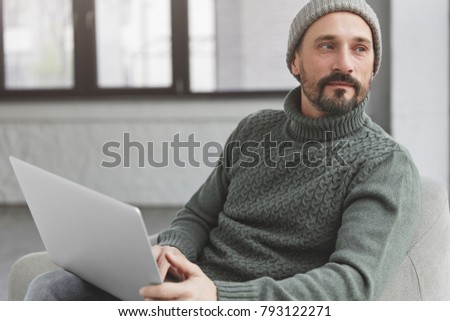 Portrait of attractive experienced contemplative businessman ponders on creative ideas for project, wait for training webinar online, sits in loft office alone. Publicity area for your text.