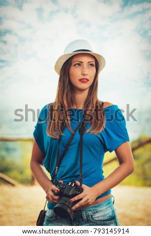 Pretty young woman standing by viewpoint and holding digital camera.