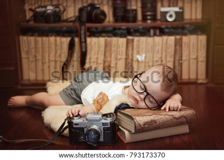 little boy, infant, sleeping on a wooden table on books with a camera in hand, library, bookshelves, retro style
