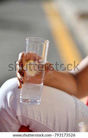 A woman with an ethnic background holds a cold drink of fresh natural water with a lemon-slice in her right Hand. 