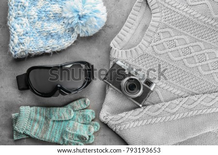 Warm clothes with photo camera and ski goggles on grey background. Winter vacation concept