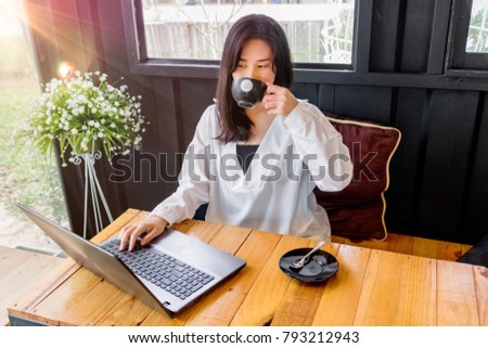 An Asian girl in white shirt plays notebook on wooden table in black room.