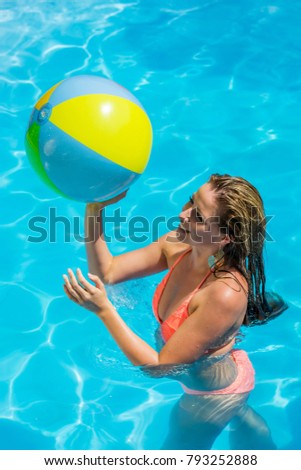Young woman plays in the pool with a beach ball