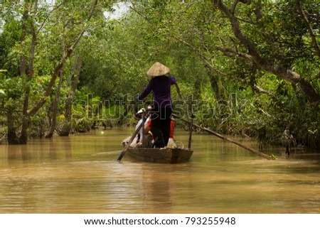 Vietnamese woman with a hat paddling in a canoe with a group of tourists in a very calm arm of the Mekong river delta surrounded by the jungle, Vietnam