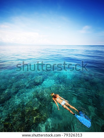 Young woman snorkeling in transparent shallow sea above coral reef.