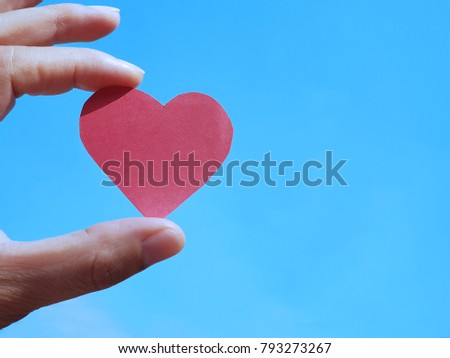 Valentine’s day. Love concept. Hand holding paper heart on blue sky background. Vintage Tone