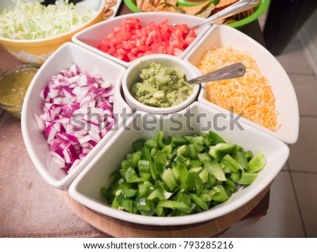 Close up photograph of a white serving tray filled with taco appetizer toppings including cheese, peppers, onion, tomato, guacamole making great background for football party or birthday celebrations.
