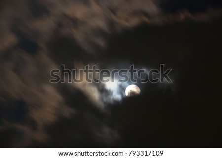 Super moon shining glowing light through the darkness of cloudy night sky; blur image for background.