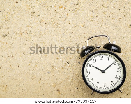 Alarm clock on beach sand, showing ten o'clock.