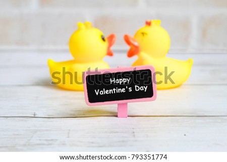 Valentine's day theme. A selective focus of blackboard written with 'Happy Valentine's Day' with a couple of yellow duck chatting at the back.