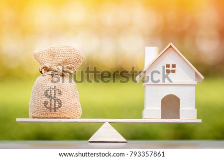 Home and money bag put on the scales with balance put on the wood in the public park, Saving for buy a new house or real estate and loan for plan business investment in the future concept.