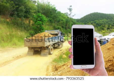 Man use mobile phone, blur image of the truck is full of lateritic soil as background.