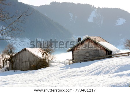 Winter landscape at early morning in Austria with snow, wooden buildings, blue sky and copy space.