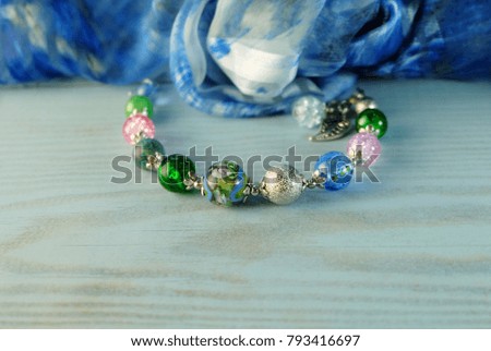 Bracelet with Murano glass and chiffon scarf lying on a blue wooden table.